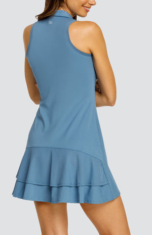 Model wearing a steel blue sleeveless dress with a quarter zip foldover collar and a double ruffle in the back.