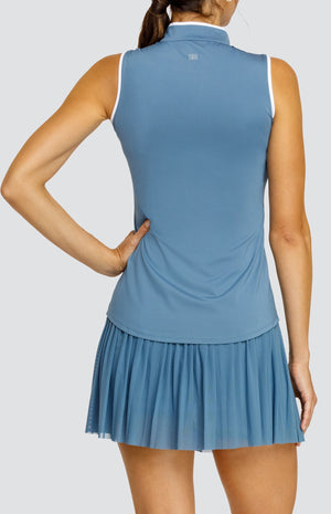 Model wearing a steel blue sleeveless top with an open v neck collar with white accents and side vents. Paired with a matching mesh pleated skort with solid undershorts.