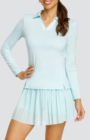 Model wearing a light blue long sleeve top with an open v neck foldover collar with white accents and side vents. Paired with a matching mesh pleated skort with solid undershorts.