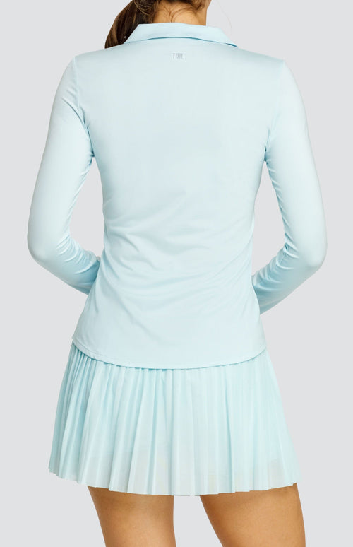 Model wearing a light blue long sleeve top with an open v neck foldover collar with white accents and side vents. Paired with a matching mesh pleated skort with solid undershorts.