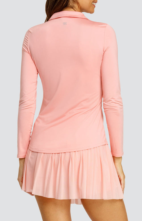 Model wearing a light pink long sleeve top with an open v neck foldover collar with white accents and side vents. Paired with a matching mesh pleated skort with solid undershorts.