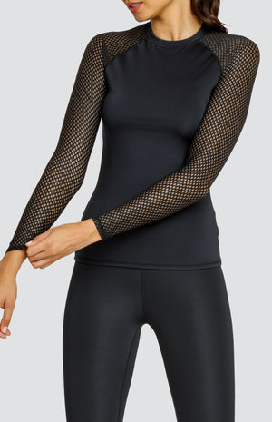 Model wearing a black crew neck shirt with raglan sleeves in a diamond mesh fabric and black high waisted leggings.