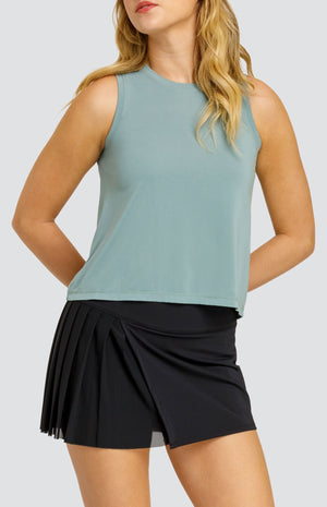 Model wearing a solid sage green hi-low swing tank top, paired with a solid black skort with a mesh asymmetrical pleat panel.
