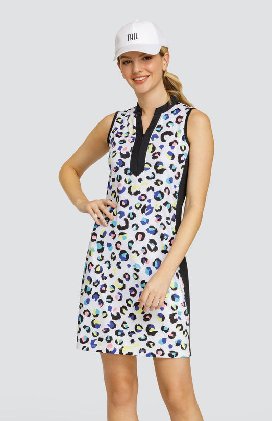 Model wearing a sleeveless dress with a spotted animal print in yellow, blue, turquoise, pink and black on a white background, and a white ball cap.