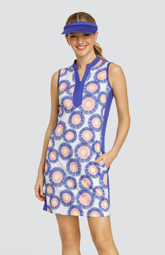 Model wearing a sleeveless dress with a circular stamp-like pattern with yellow, pink, and blue rings on a white background, with blue side inserts and a blue visor.