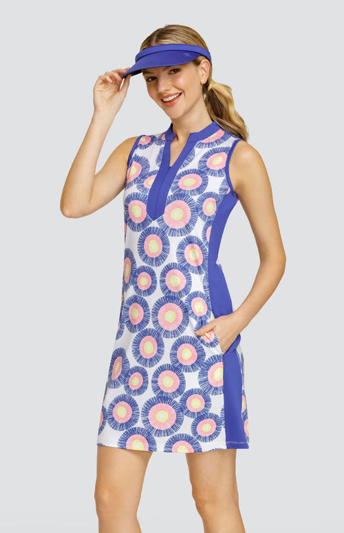 Model wearing a sleeveless dress with a circular stamp-like pattern with yellow, pink, and blue rings on a white background, with blue side inserts and a blue visor.