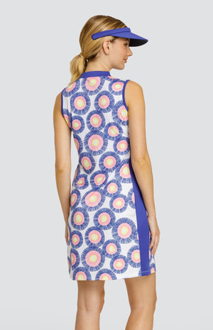 Model wearing a sleeveless dress with a circular stamp-like pattern with yellow, pink, and blue rings on a white background, with blue side inserts and a blue visor.