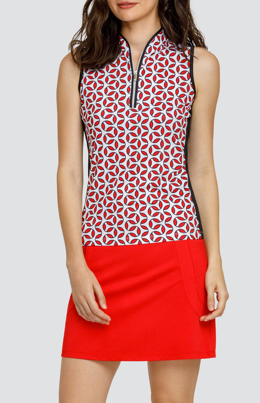 Model wearing a sleeveless golf top with a red and white geometric print, and a red skort.