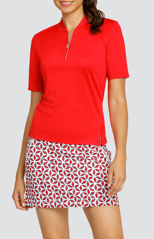 Model wearing a short sleeve red golf top and a skort with a red and white geometric print.