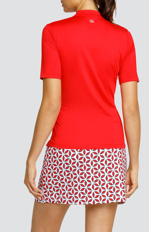 Model wearing a short sleeve red golf top and a skort with a red and white geometric print.