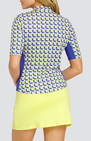 Model wearing an elbow sleeve golf top with a geometric circular pattern in blue and yellow on a white background, and a solid yellow pull-on golf skort.