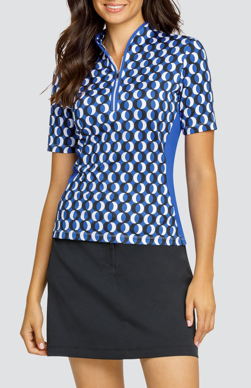 Model wearing a short sleeve golf top with a circular blue, white, and black pattern, and a black skort.