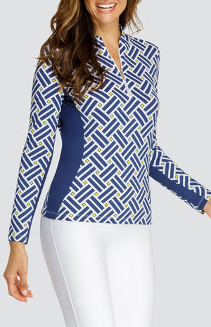 Model wearing a long sleeve quarter zip gold top with a blue criss cross pattern and yellow squares on a white background, with solid white pull on pants.