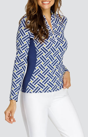 Model wearing a long sleeve quarter zip gold top with a blue criss cross pattern and yellow squares on a white background, with solid white pull on pants.