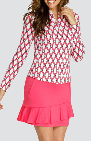 Model wearing a long sleeve quarter-zip golf top with a pink and white lattice pattern and a pull on pink golf skort with a flounce insert.