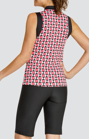 Model wearing a sleeveless quarter-zip golf top with a pink, white and black geometric pattern and black sleeve inserts, and pull on black golf shorts.