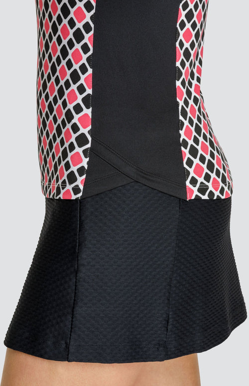 Close up of the mock layered side inserts on a sleeveless quarter-zip golf top in a black and pink diamond pattern with black side inserts, and a textured pull on black golf skort.