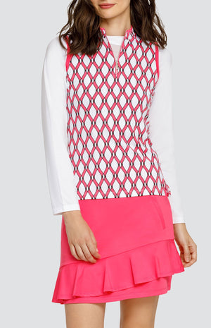 Model wearing a white long sleeve layering crop top under a sleeveless quarter-zip golf top with a pink and white lattice pattern, and a pull on pink golf skort with a flounce hem.