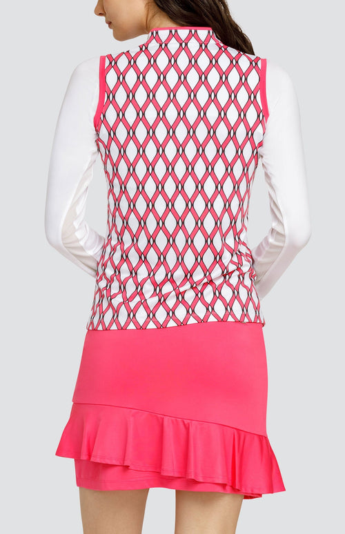 Model wearing a white long sleeve layering crop top under a sleeveless quarter-zip golf top with a pink and white lattice pattern, and a pull on pink golf skort with a flounce hem.