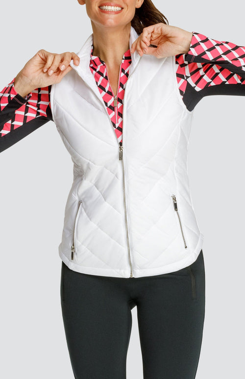 Model wearing a white puffer vest over a long sleeve quarter-zip golf top with a pink 3-dimensional block pattern and pull on black golf pants.