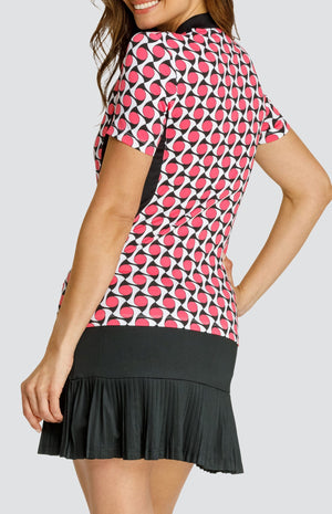 Model wearing a short sleeve quarter-zip golf top with a pink, white and black geometric pattern and black inserts, with a black pleated golf skort.