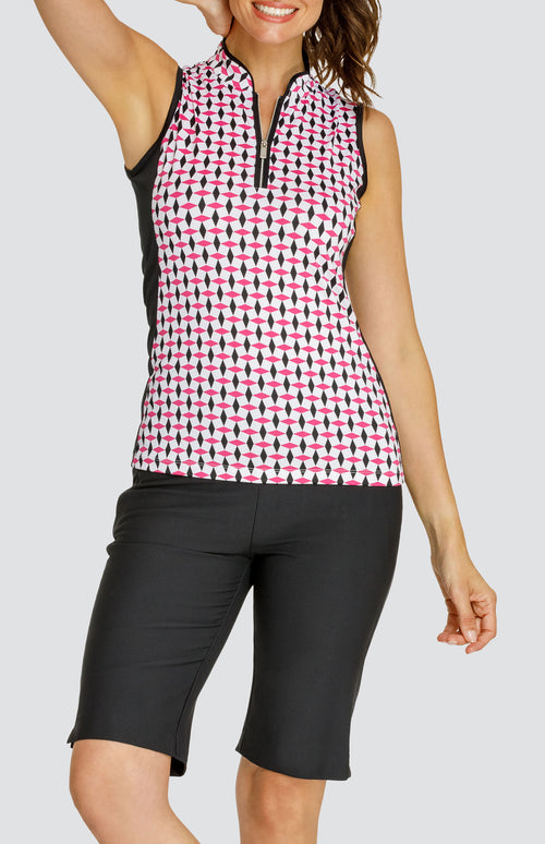 Model wearing a sleeveless quarter-zip golf top in a pink and black geometric alternating diamond print on a white background with black side inserts, paired with solid black pull-on golf shorts.