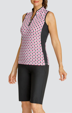 Model wearing a sleeveless quarter-zip golf top in a pink and black geometric alternating diamond print on a white background with black side inserts, paired with solid black pull-on golf shorts.