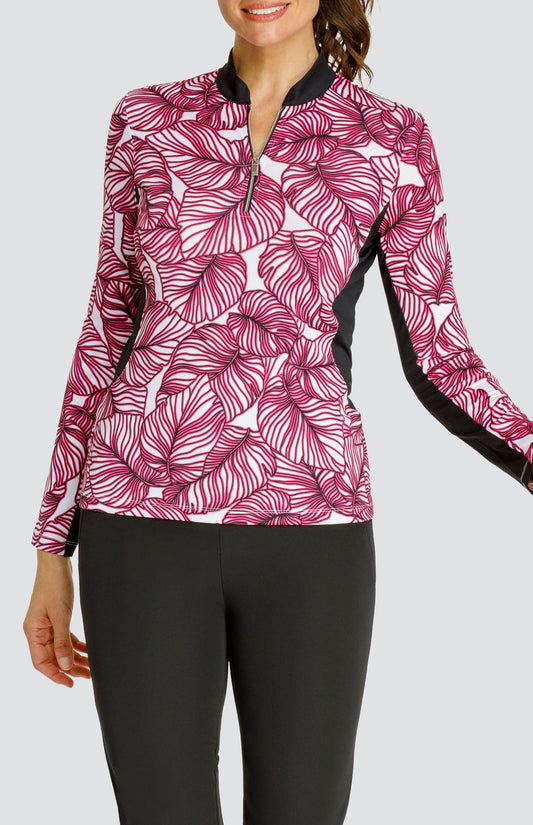 Model wearing a long sleeve quarter-zip golf top in a pink frond print on a white background with black side and underarm inserts, paired with a solid black pull-on golf pant.