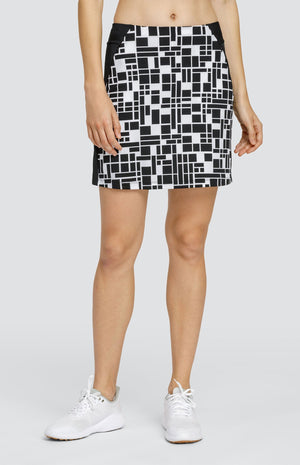 Model wearing a pull-on golf skirt with a black and white rectangular geometric pattern with black side inserts.