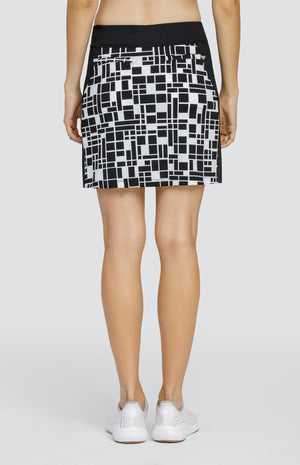 Model wearing a pull-on golf skirt with a black and white rectangular geometric pattern with black side inserts.