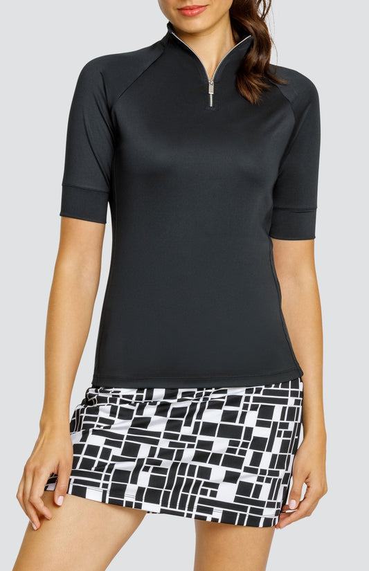 Model wearing a short sleeve black golf top and a black and white geometric printed skort.