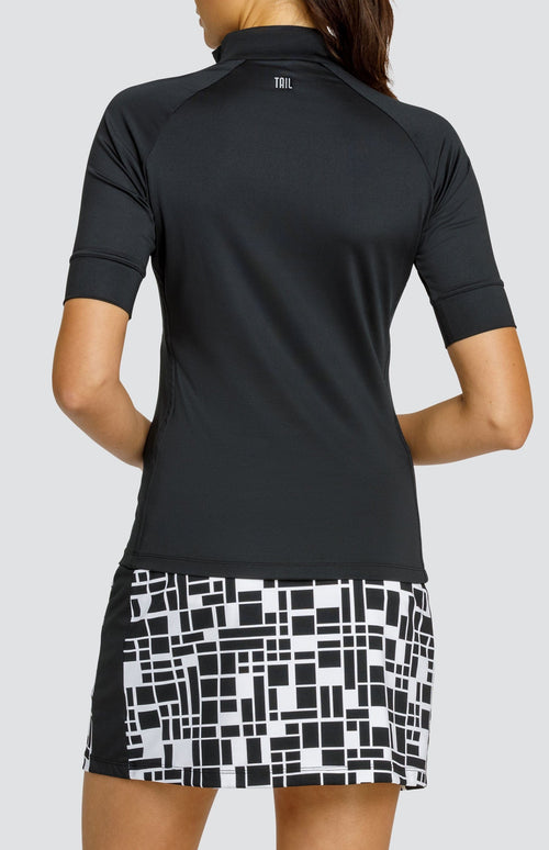 Model wearing a short sleeve black golf top and a black and white geometric printed skort.