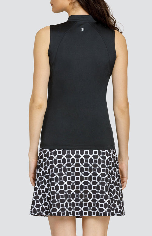 Model wearing a sleeveless black golf top and a golf skort with a black and white geometric pattern.