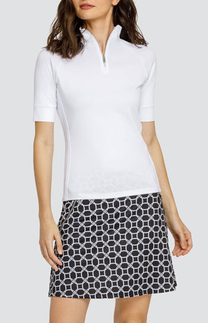 Model wearing a short sleeve white golf top and a black and white geometric print skort.