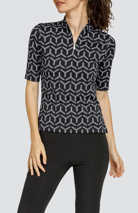 Model wearing a mid sleeve golf top with a black and white geometric print, and black pants.