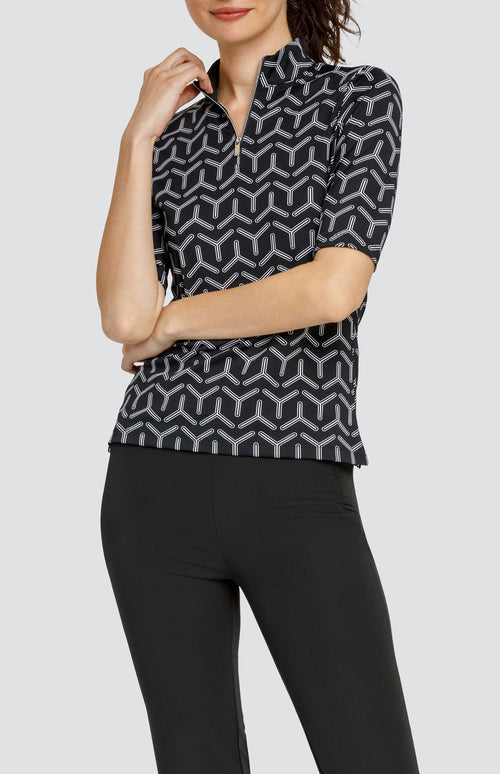 Model wearing a mid sleeve golf top with a black and white geometric print, and black pants.