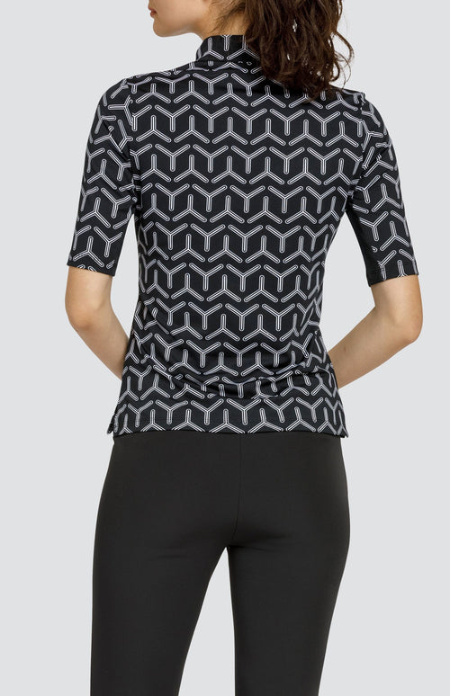 Model wearing a mid sleeve golf top with a black and white geometric print, and black pants.