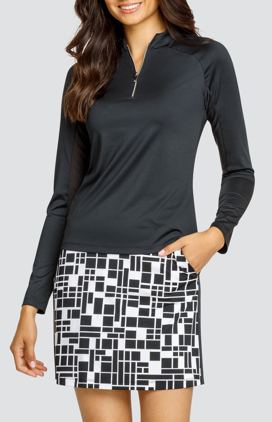 Model wearing a black raglan long sleeve golf top and a skort with a geometric black and white print.