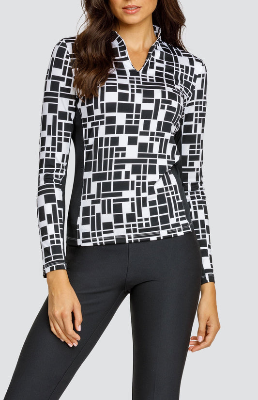Model wearing an open V-neck golf top with long sleeves in a black and white geometric print with black side inserts.