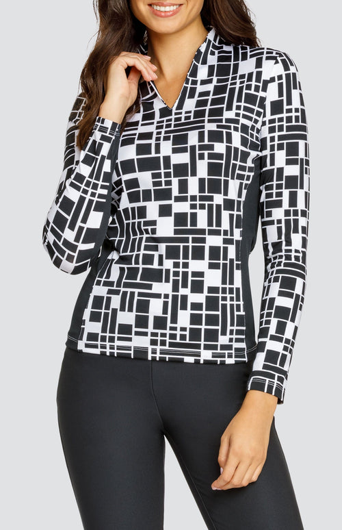 Model wearing an open V-neck golf top with long sleeves in a black and white geometric print with black side inserts.