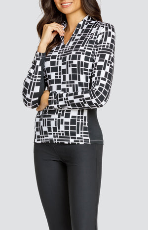 Model wearing an open V-neck golf top with long sleeves in a black and white geometric print with black side inserts.