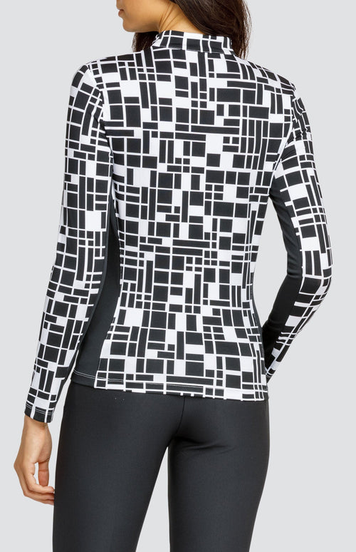 Model wearing an open V-neck golf top with long sleeves in a black and white geometric print with black side inserts.