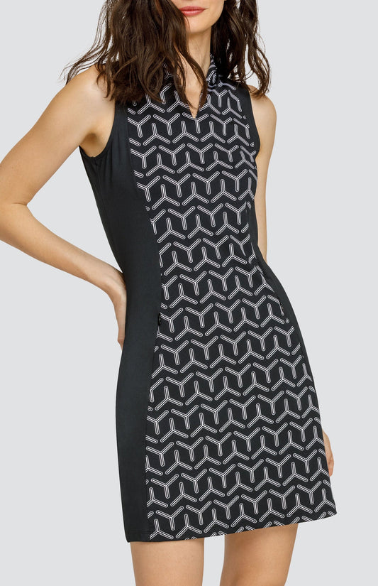 Model wearing a sleeveless golf dress with a black and white geometric print with alternating three-point shapes and black side inserts