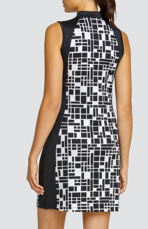 Model wearing a sleeveless golf dress in a geometric print with black and white rectangles, and black side inserts.
