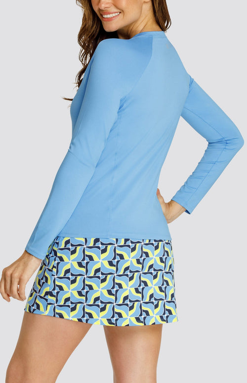 Model wearing a light blue long sleeve tennis top and a skort with light blue and neon yellow abstract grid pattern.